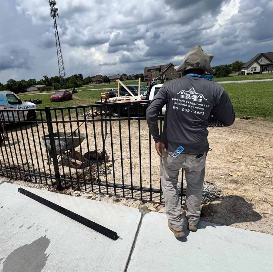 Construction worker by a partially installed black fence, cloudy sky, open field.