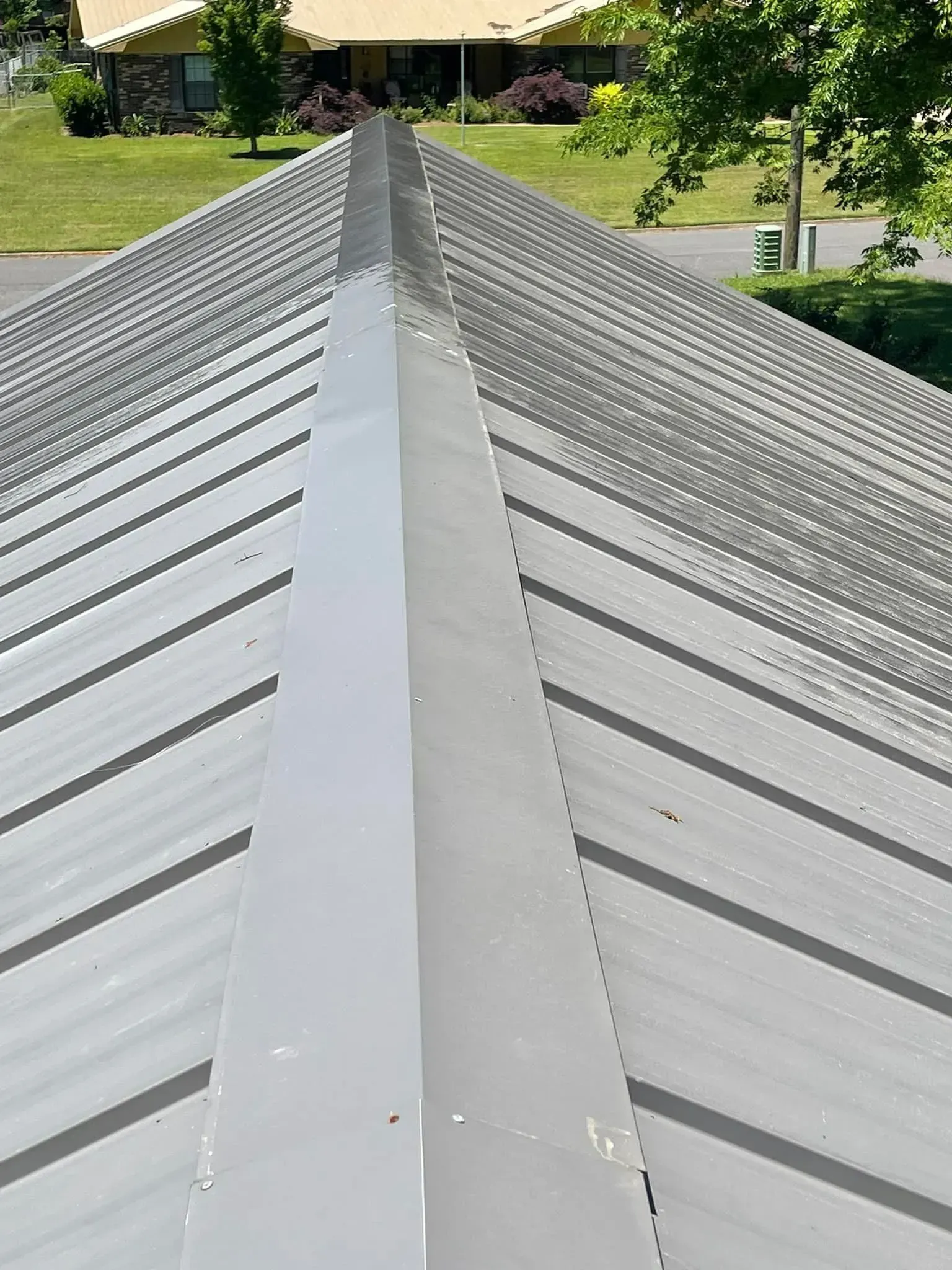 Close-up of a metal roof with a central ridge. The color is silver, and the setting appears to be outdoors.