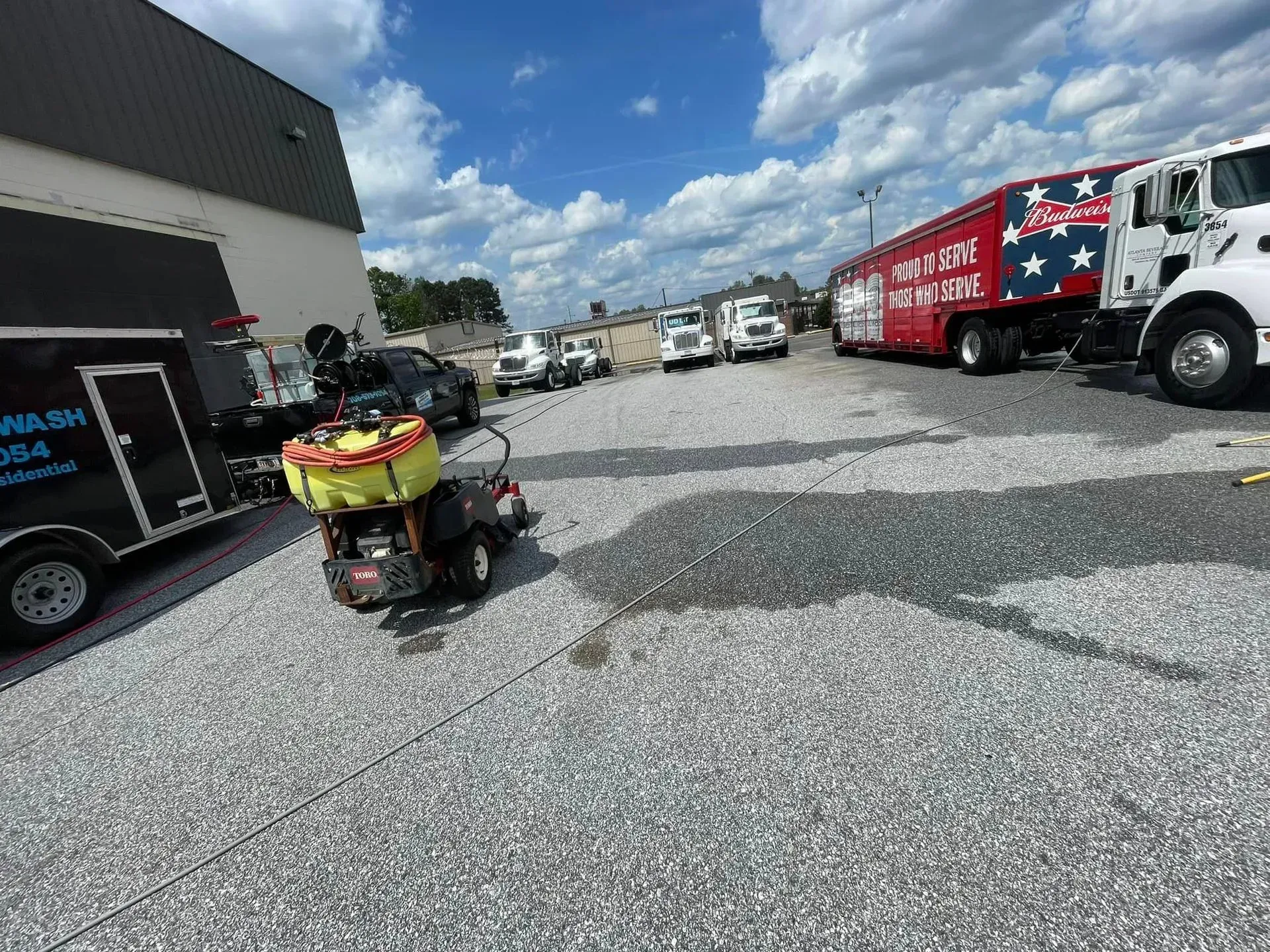 A golf cart with a yellow container, multiple emergency vehicles parked on a gravel lot under a cloudy blue sky.
