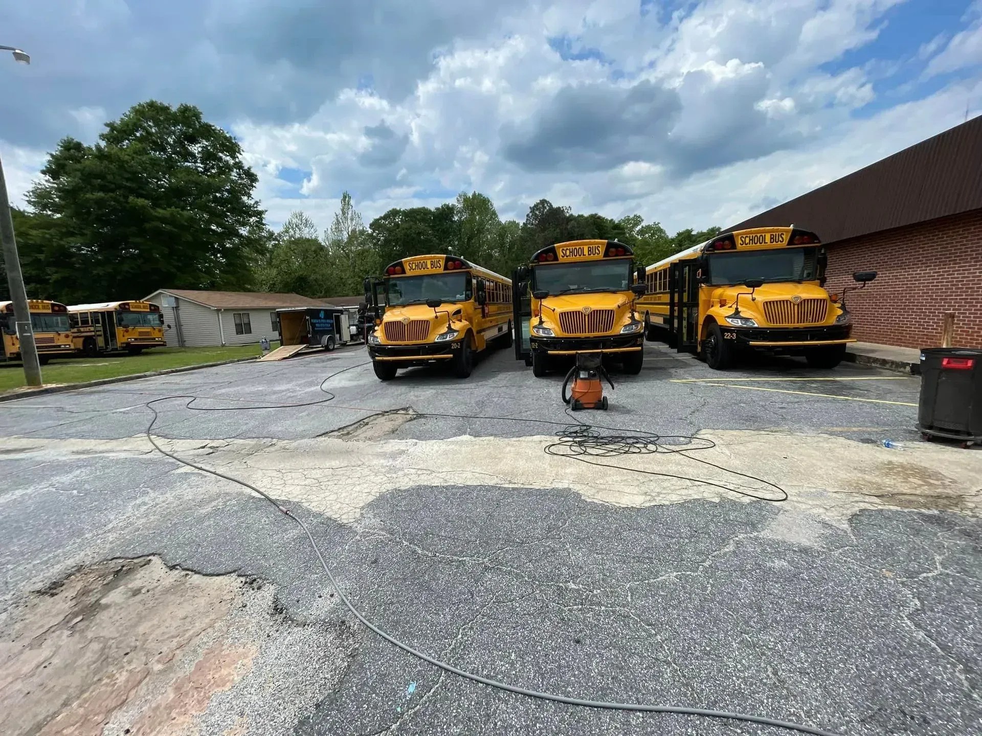 Three yellow school buses parked on a gray surface in front of a building under a cloudy sky.