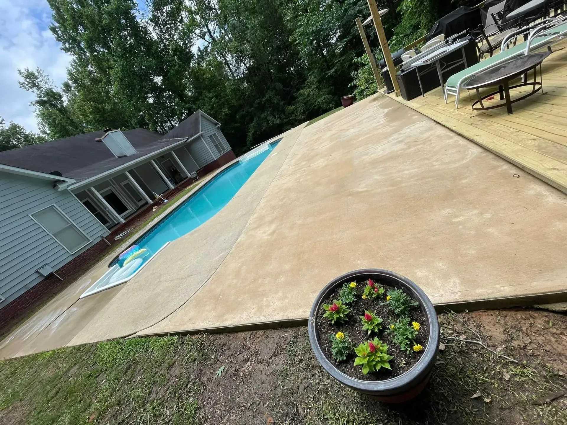 Poolside view of a house with a pool covered, potted flowers in foreground, trees in the background.