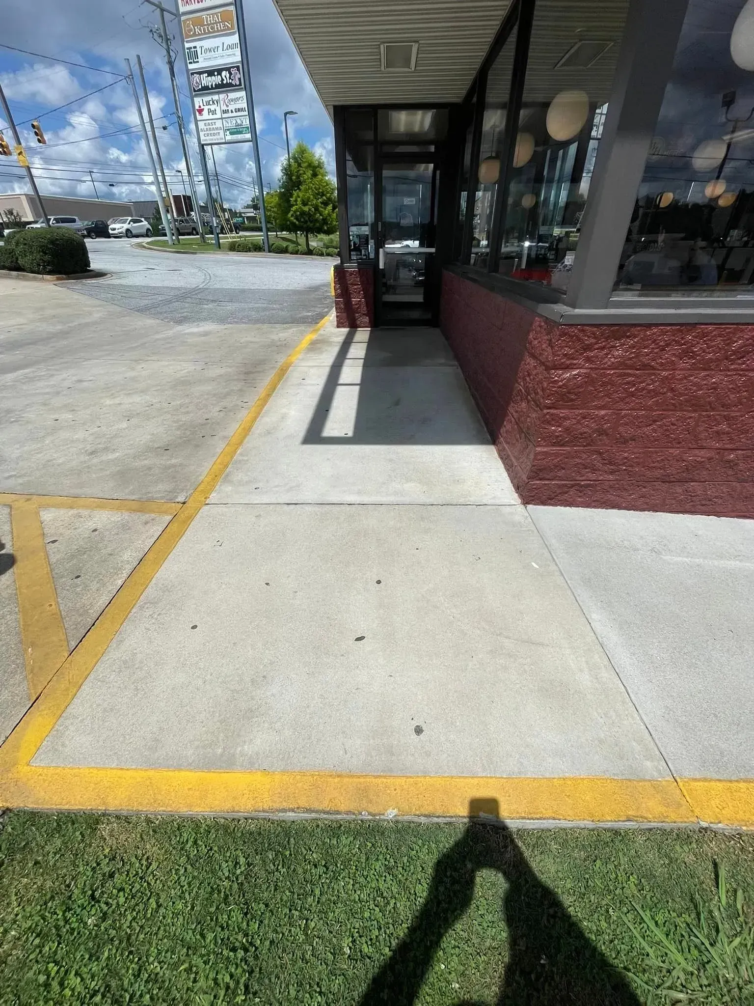 Sidewalk next to a building, yellow parking lines and grassy area visible.