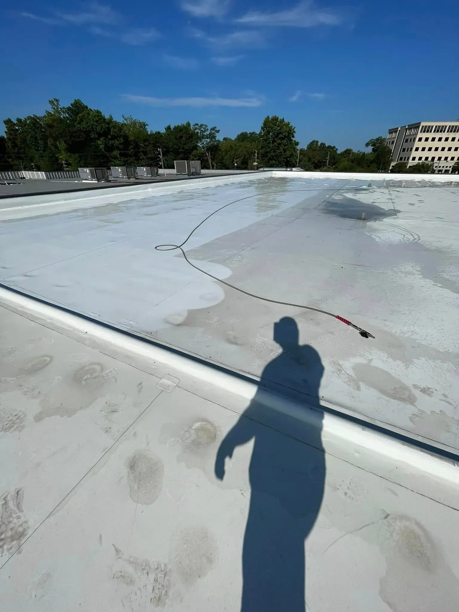 Shadow of a person on a flat, white roof with a string of red and white objects. Blue sky overhead.