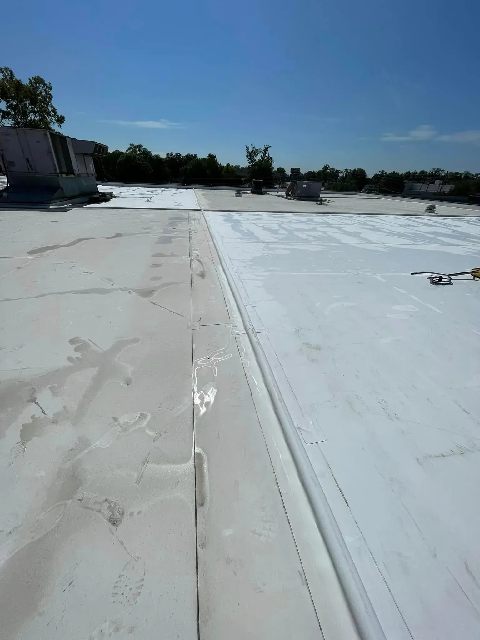 White commercial roof with visible seams, vents, and blue sky.