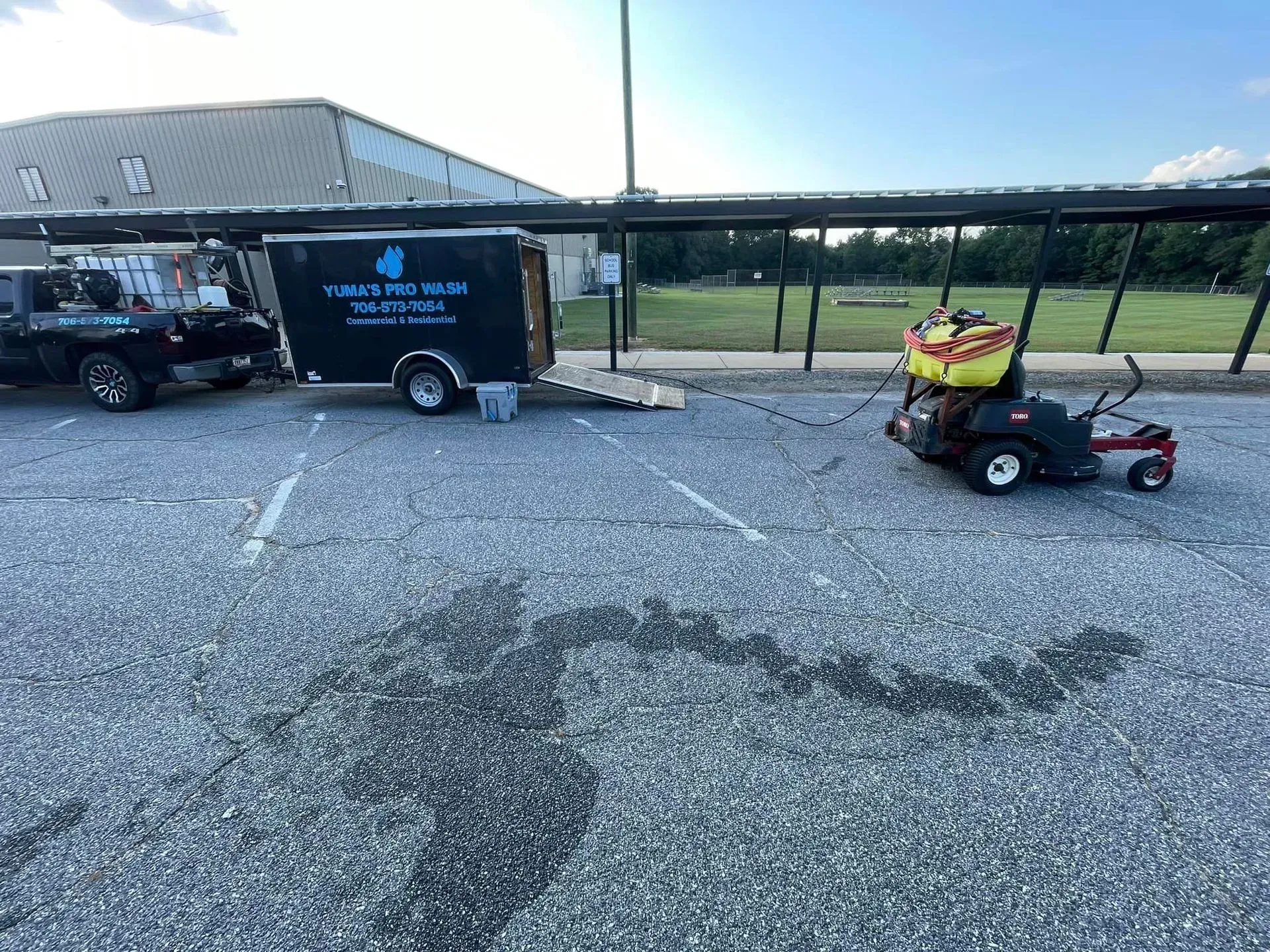 A black pickup truck, trailer, and riding lawnmower parked on asphalt. A banner on the trailer reads 
