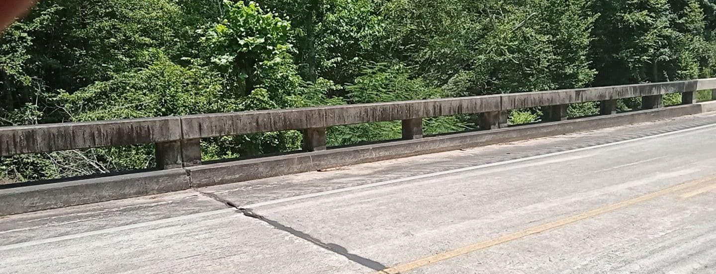 A concrete bridge with a textured road in the foreground, and lush green trees in the background.