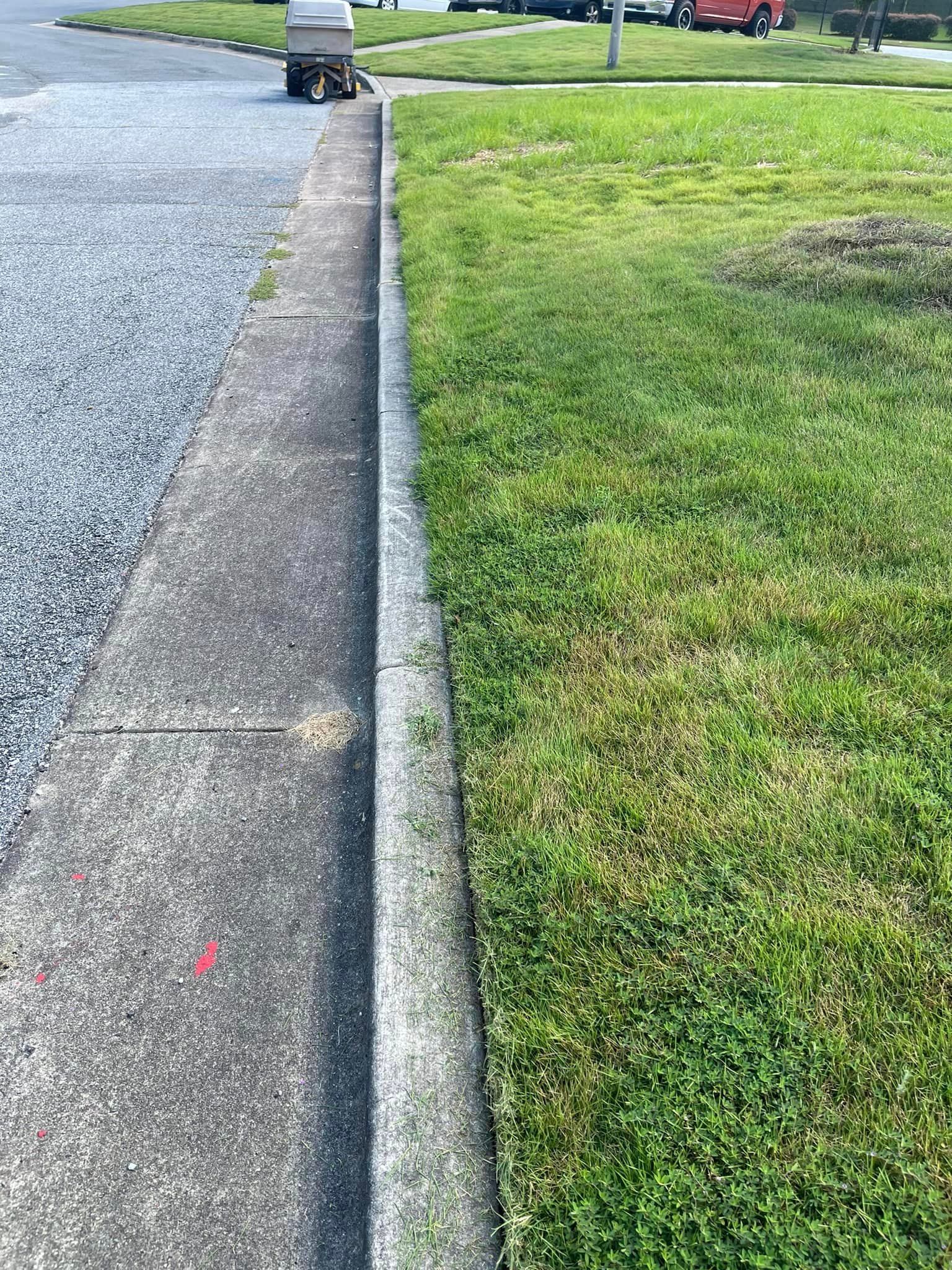 Concrete curb separating gravel sidewalk and grassy lawn.