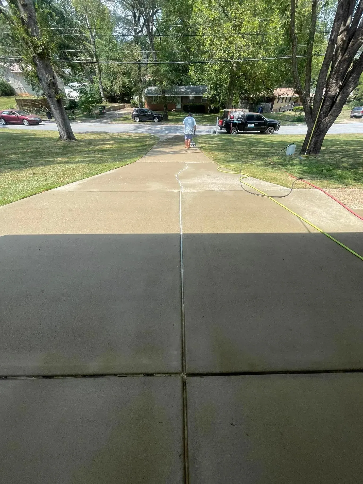 Person walking down a driveway with a straight line, car and boat in the background, sunny day.