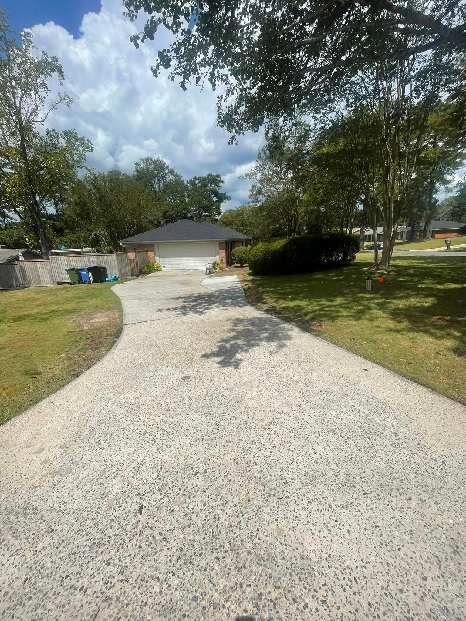 Driveway leading to a one-story house with a two-car garage under a partly cloudy sky.
