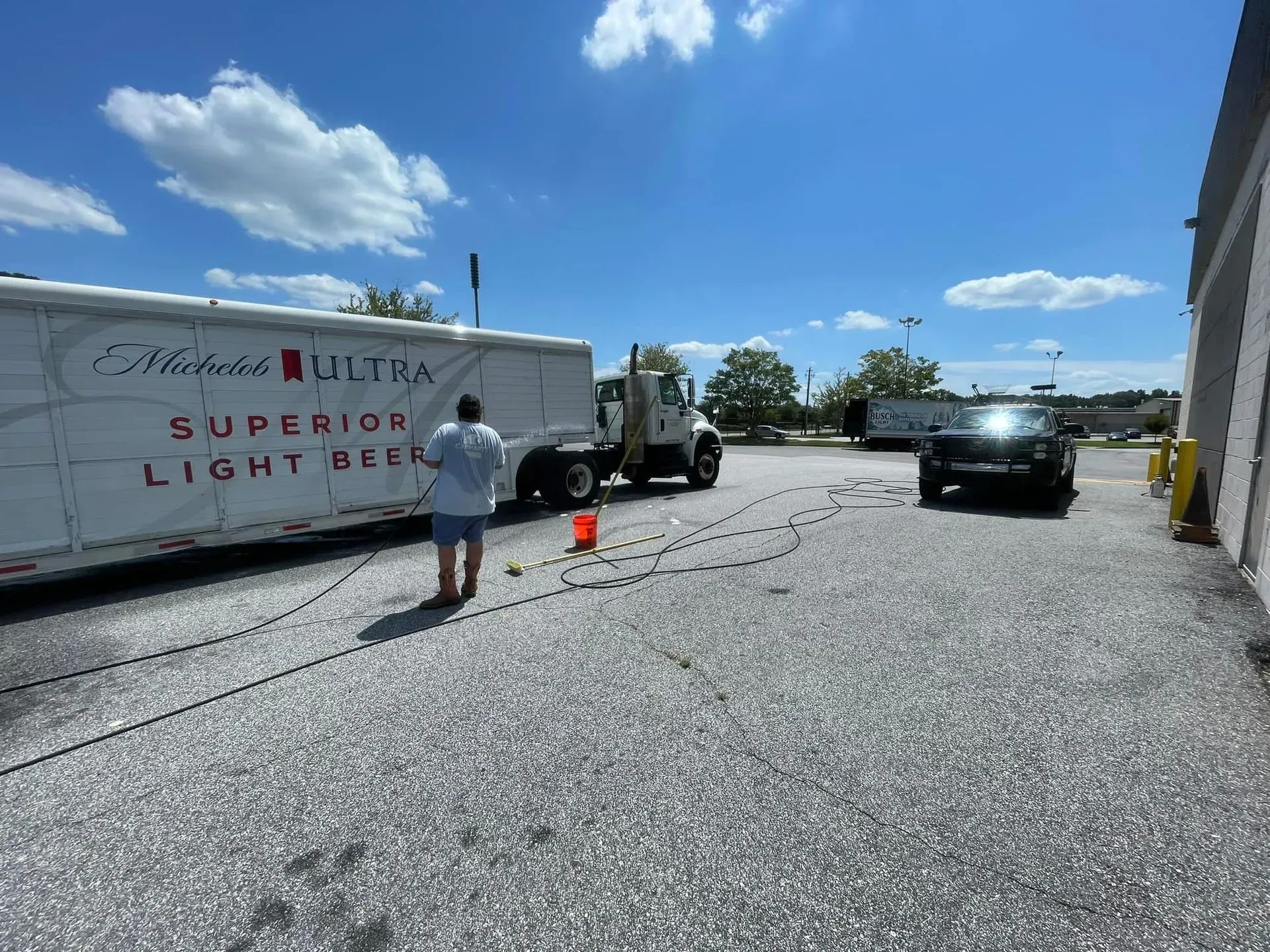 A person stands near a semi-truck with a Michelob Ultra trailer in a parking lot on a sunny day.