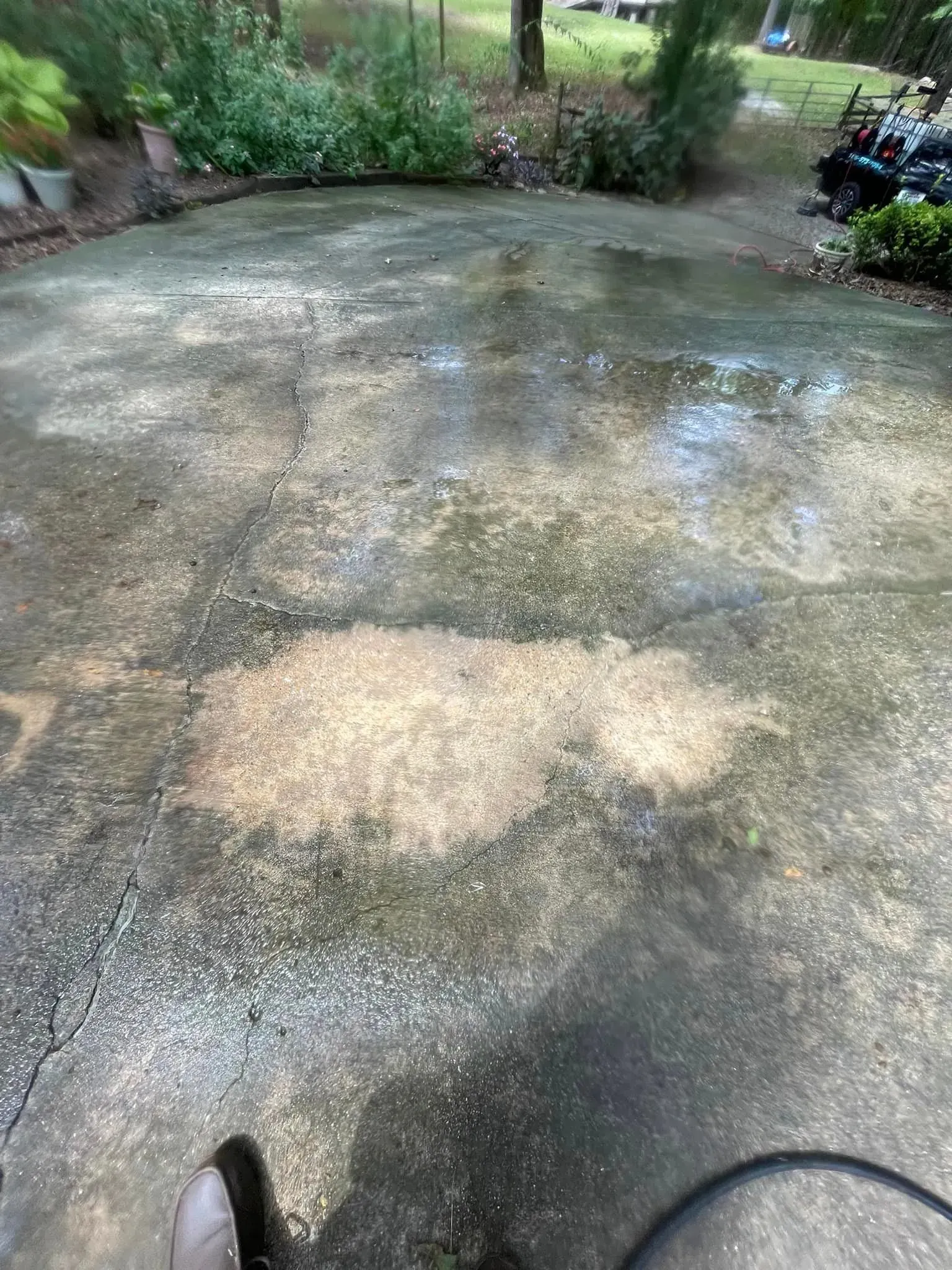 Concrete patio with discoloration, cracks, and standing water. Part of a shoe and object visible at the bottom.