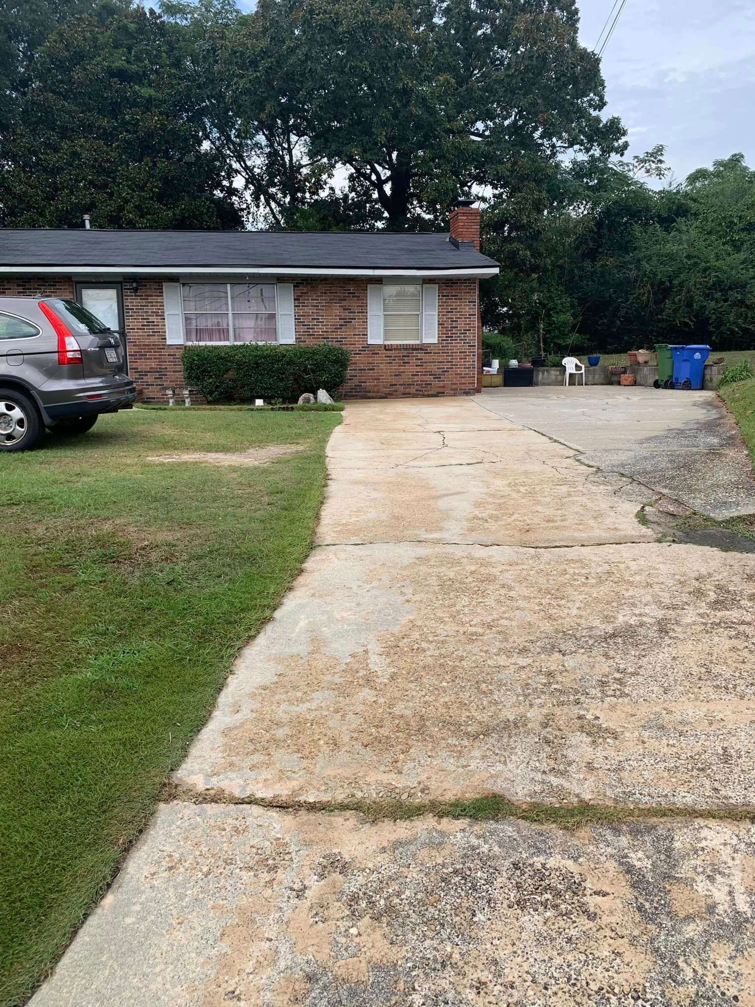 Driveway leading to a brick house with a dark car parked on the side.
