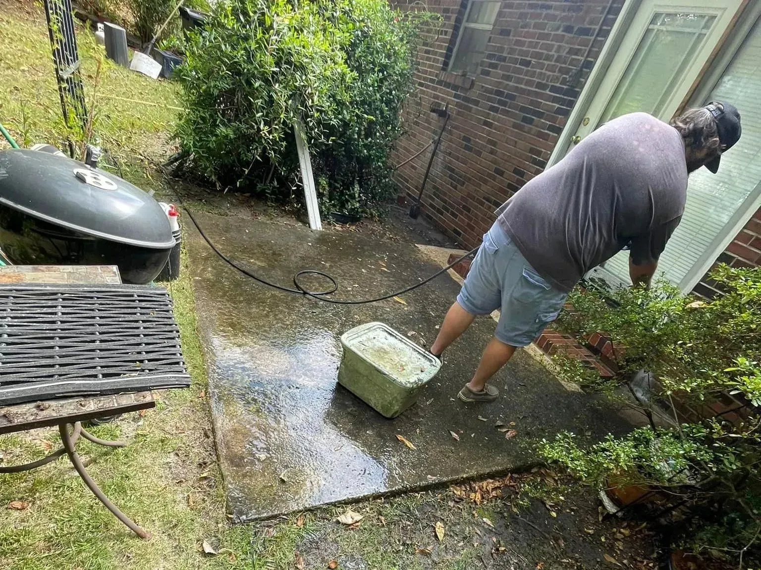Person pressure washing a concrete patio next to a brick building.