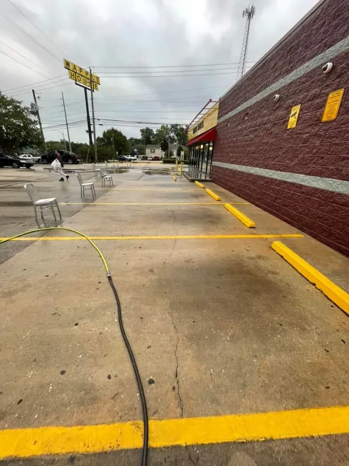 Exterior of a brick building with yellow parking space lines. A hose runs across the concrete sidewalk. Cloudy sky.