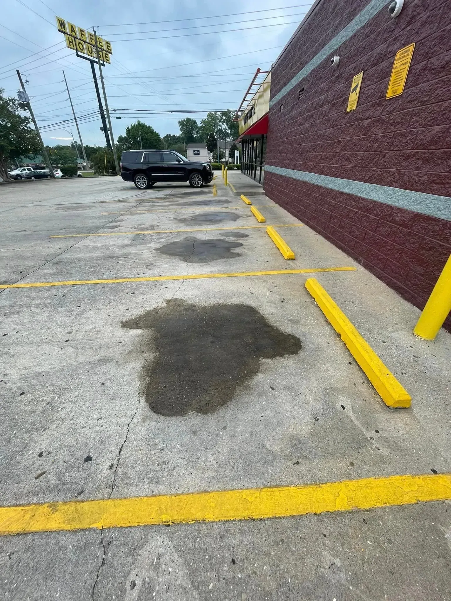 Puddles of water in a parking lot next to a brick building and yellow parking bumpers; a black truck is parked.