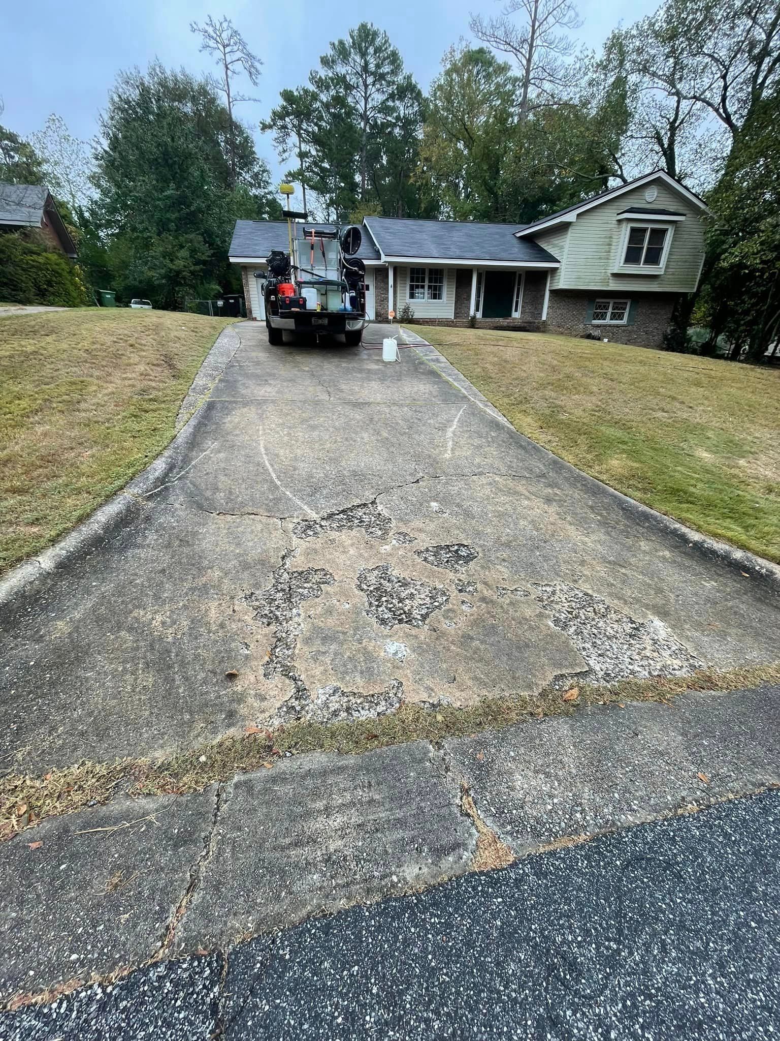 Cracked asphalt driveway leading to a house with a vehicle parked on it; overcast day.