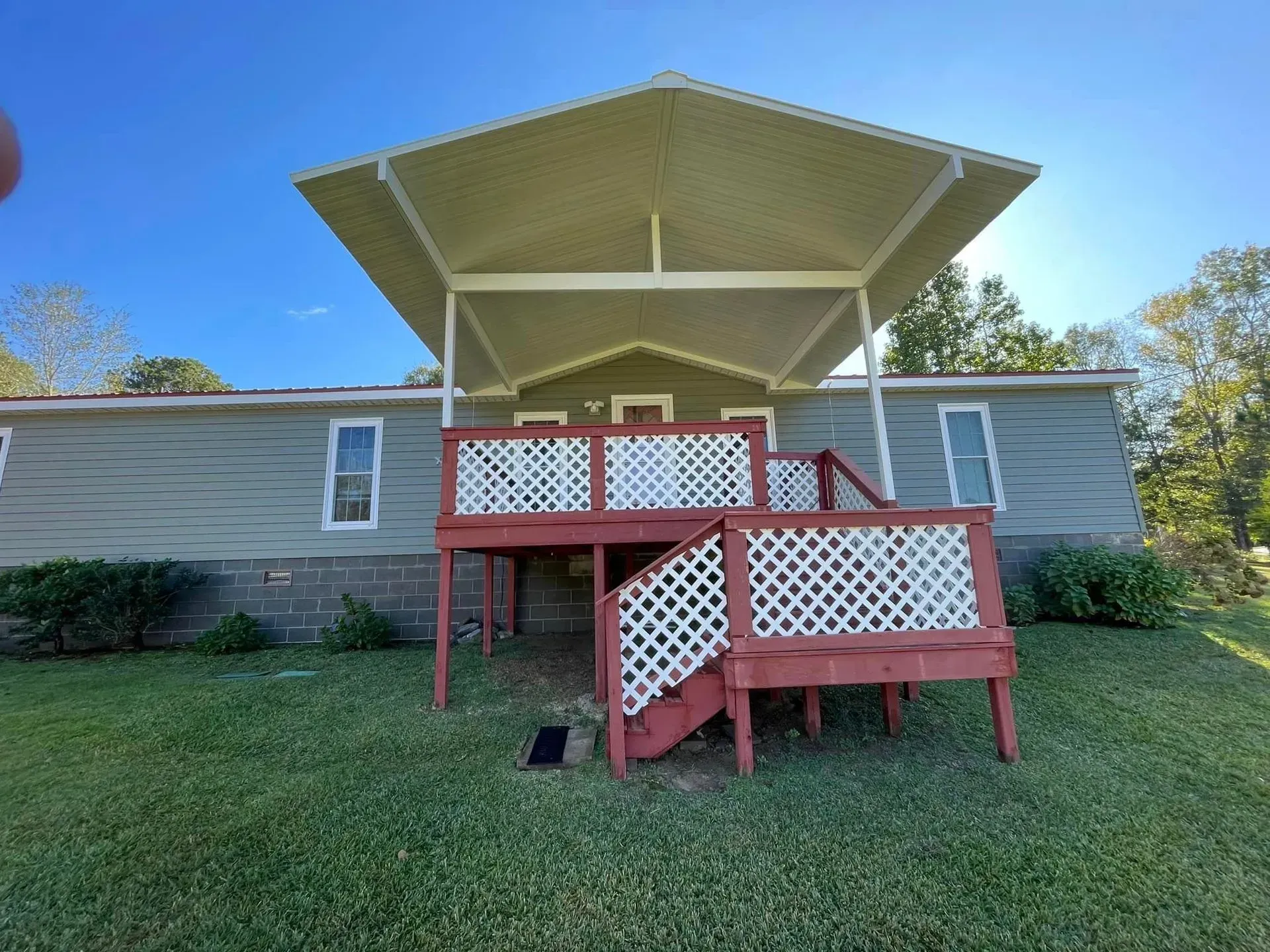 House with red deck, lattice railings, and white canopy roof. Green siding, blue sky, and grass.