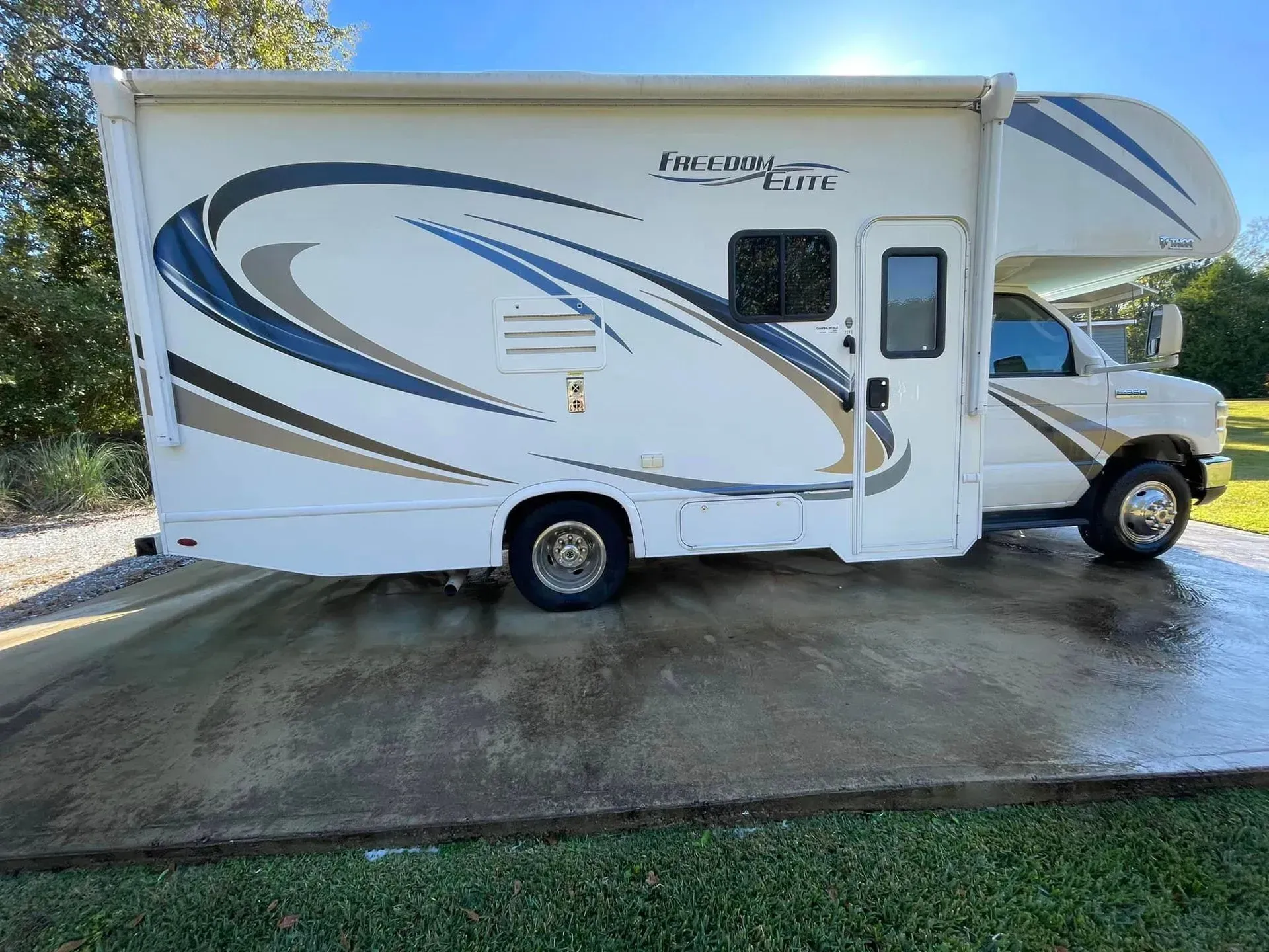 White RV parked on a concrete surface, with blue and tan graphics. Sunny day.