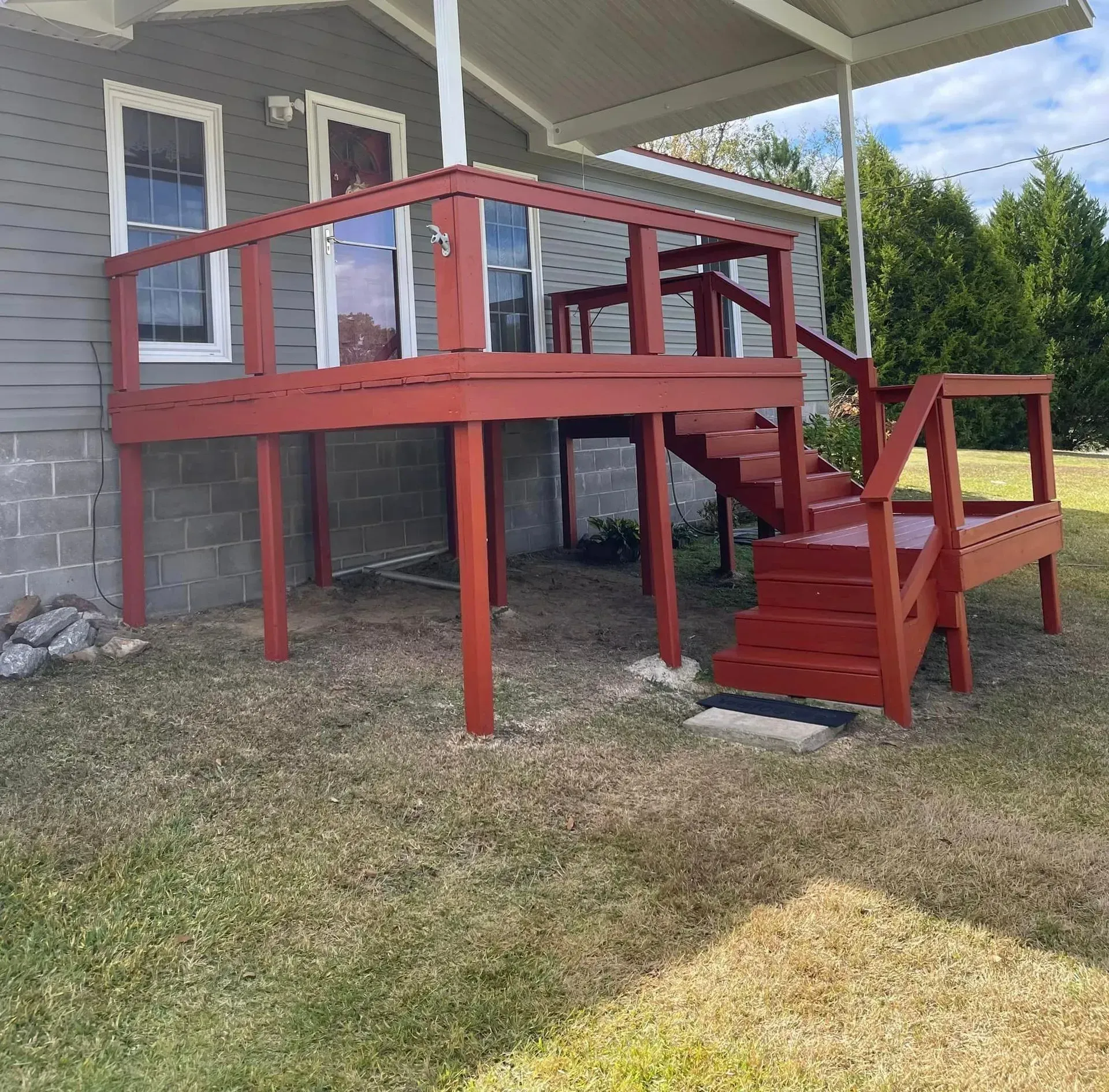 Red wooden deck with stairs attached to a gray house, set over cinder blocks.