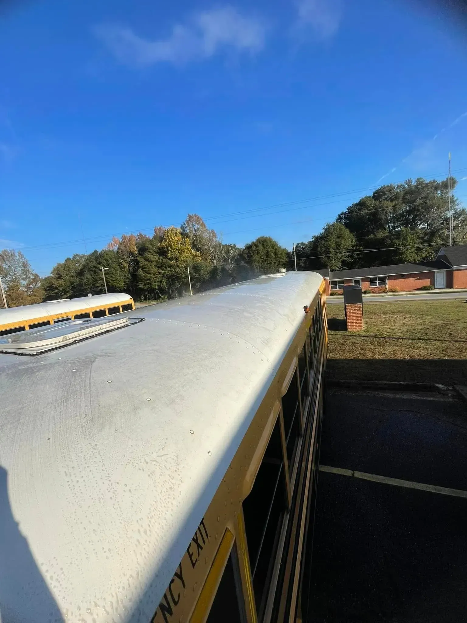 Side view of a yellow school bus parked outside on a sunny day. A building is visible in the background.