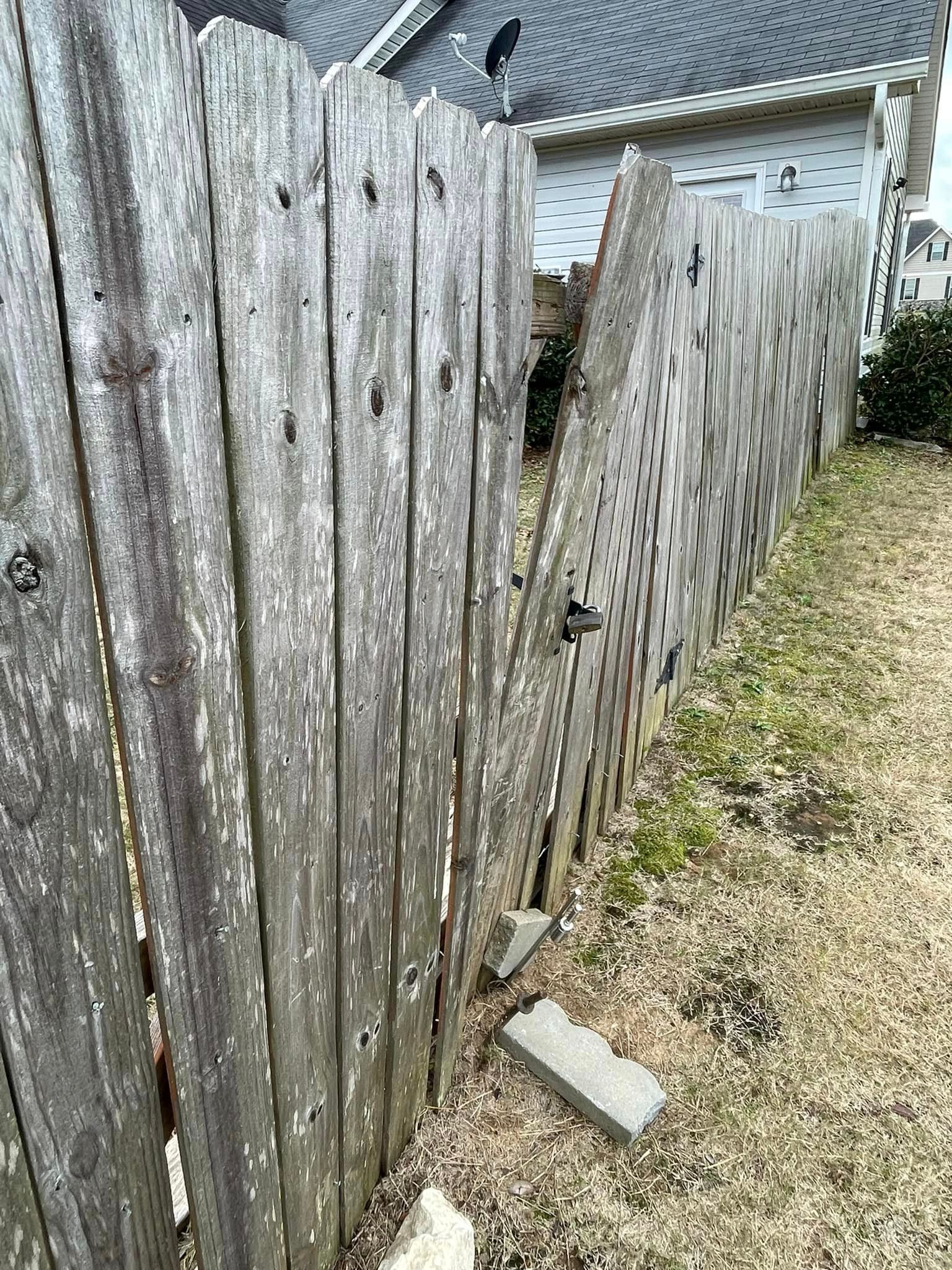 Broken weathered wooden fence in a yard, leaning.