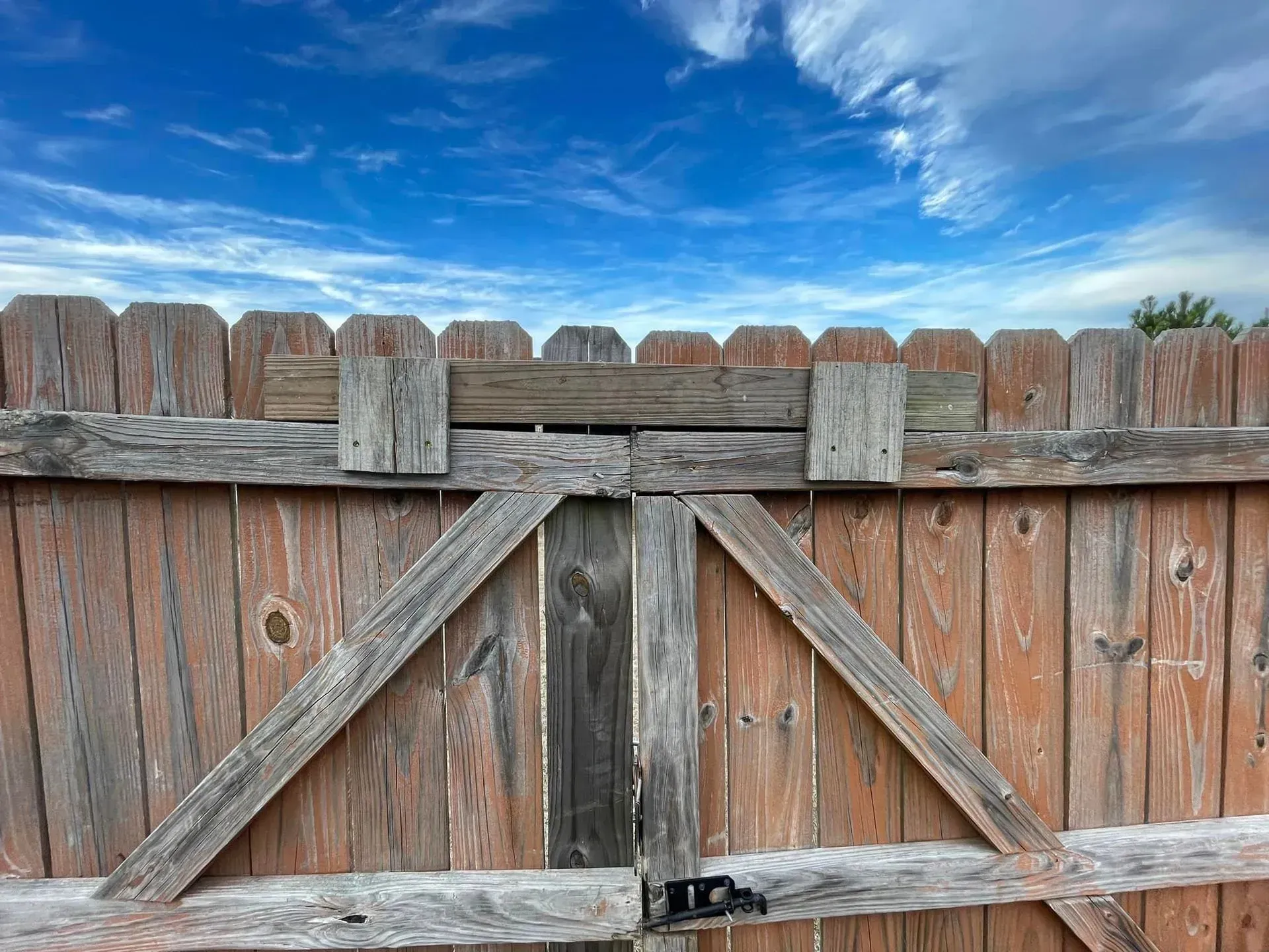 Wooden gate, weathered with gray and brown tones, against a blue sky with streaky clouds.