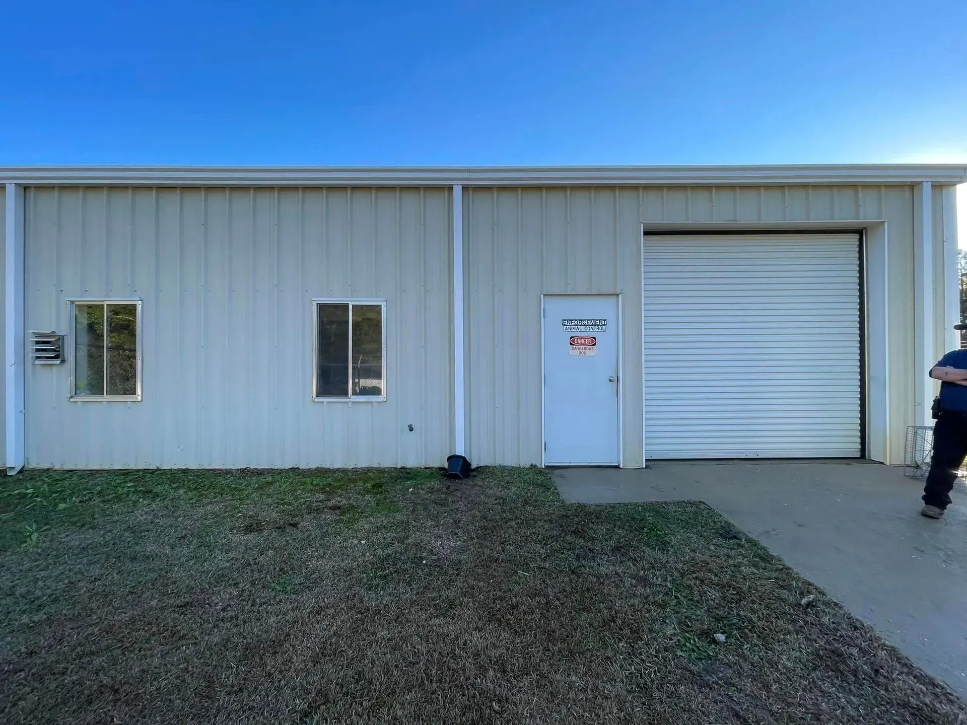 Exterior of a light-colored commercial building with a roll-up door, two windows, and a white door.