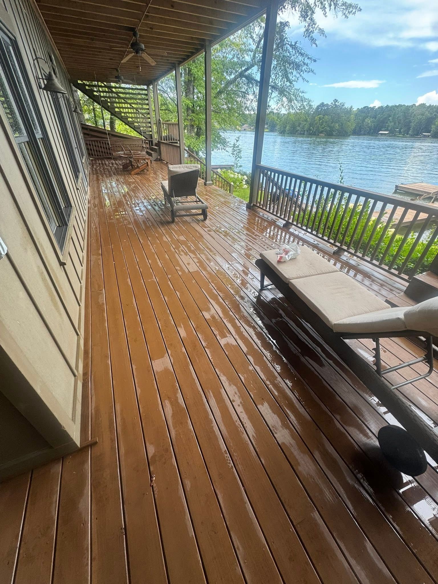 Wooden deck with lake view, wet from rain. Lounge chairs, railing, and covered walkway.