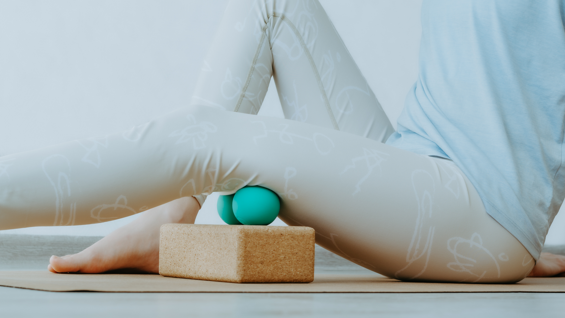 A person is sitting on a yoga mat with a massage ball on their leg.