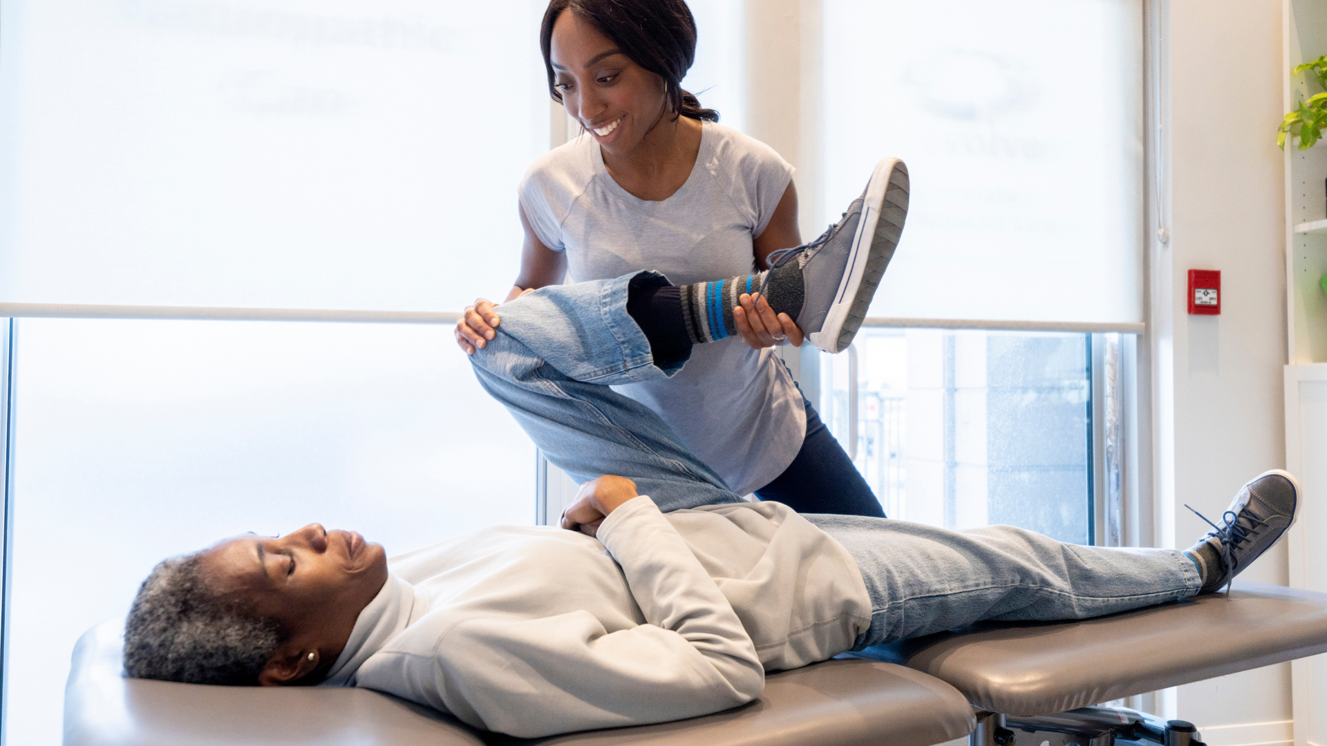 A woman is stretching a patient 's leg on a table.