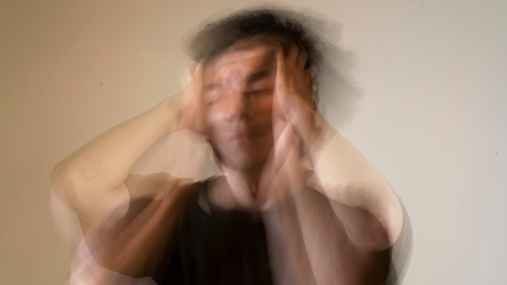 Man with hands on head, blurred effect suggests stress or headache.