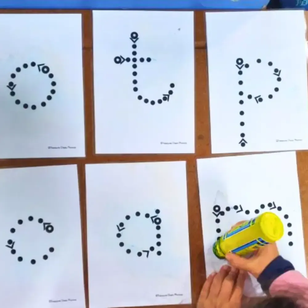 Child tracing dotted letters with a marker on printed worksheets. Letters: o, t, p, c, a, and n.