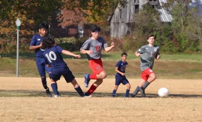 Soccer players in dark and gray jerseys chase a ball on a grassy field.