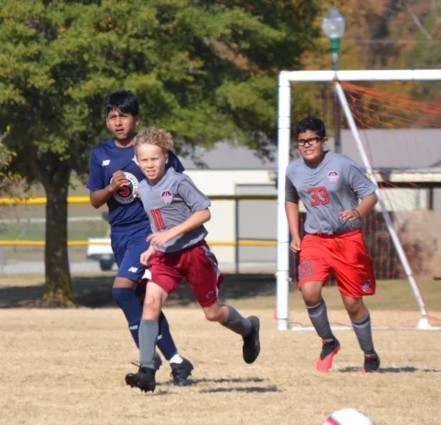 Soccer players running on a field, with one in gray and red dribbling the ball during play