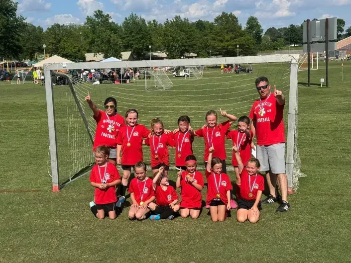 Youth soccer team in red jerseys posing on a grassy field in front of a goal.