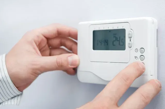 Une personne utilise un thermostat pour régler la température à 24 degrés