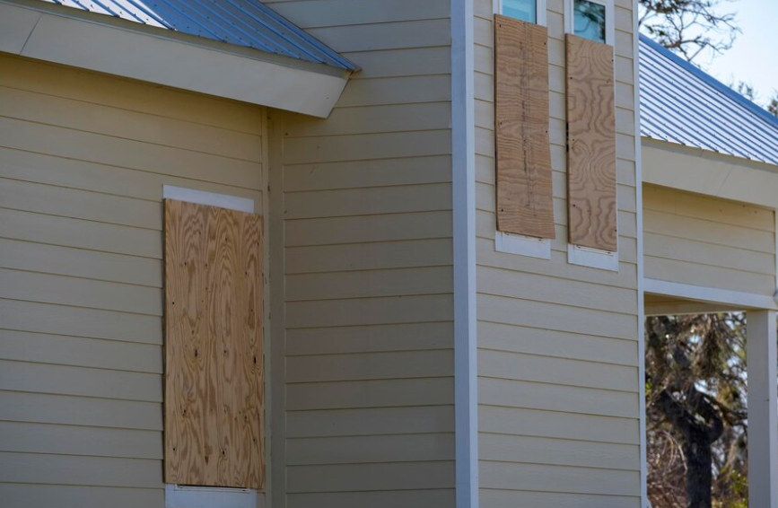 The windows of a house are boarded up with plywood.