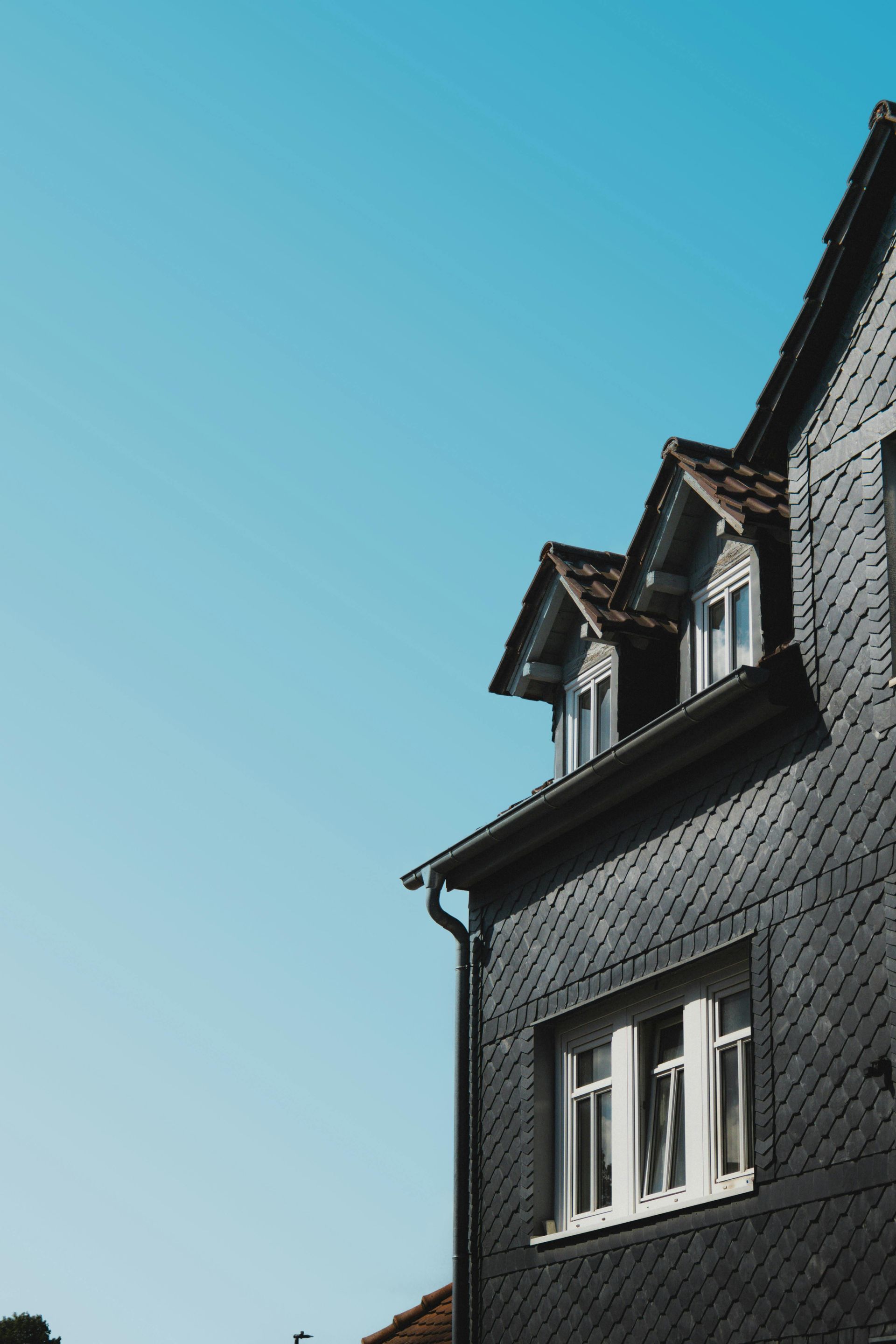 Dark building with dormer windows against a clear blue sky.