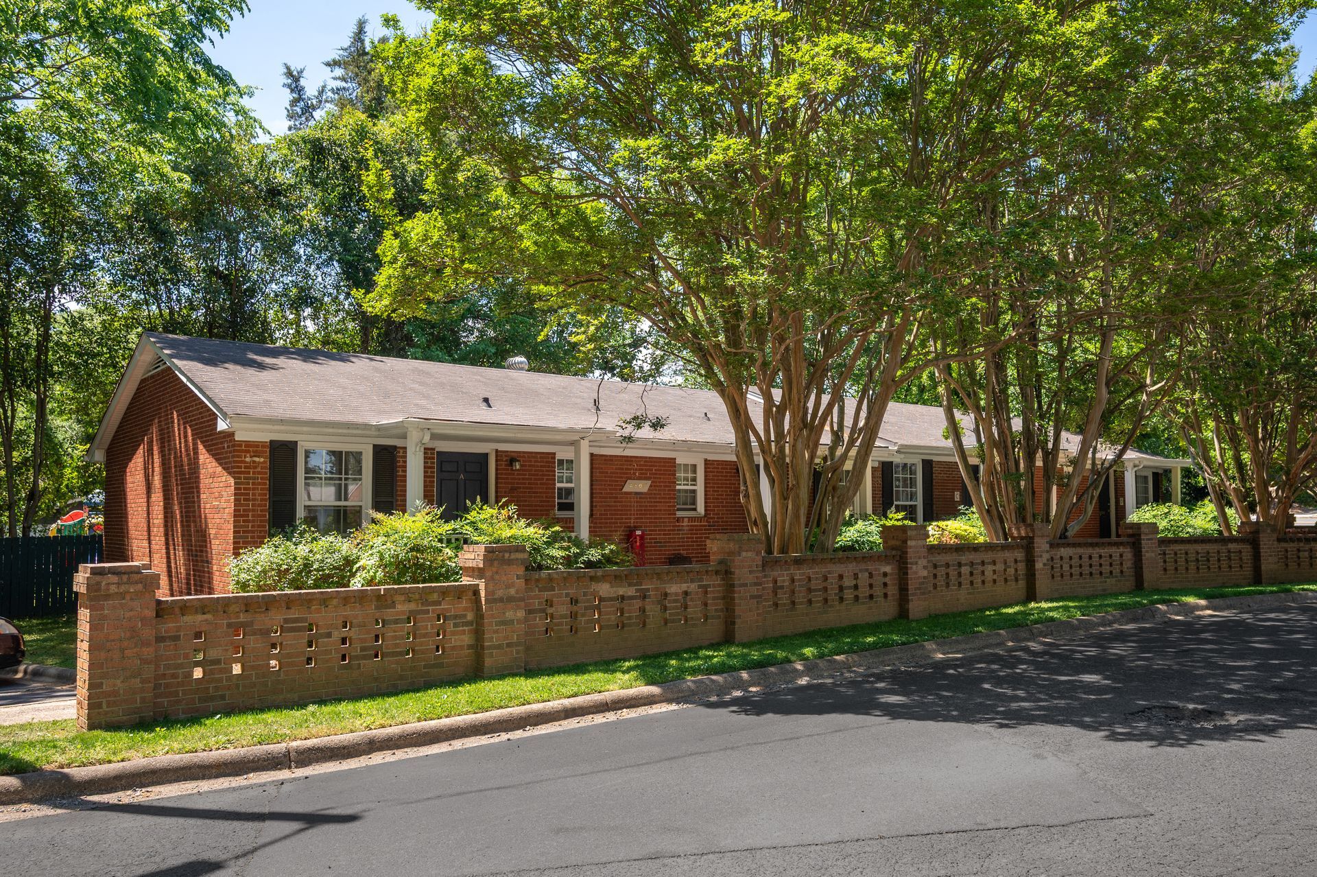 Brick apartment building with balconies, surrounded by trees and grass, on a sunny day.