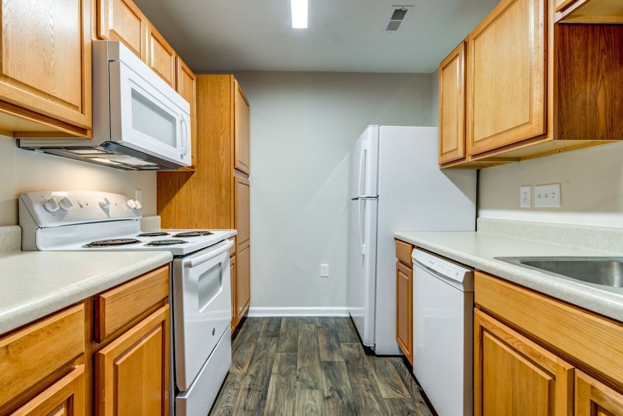 Kitchen with light wood cabinets, white appliances, and gray flooring.