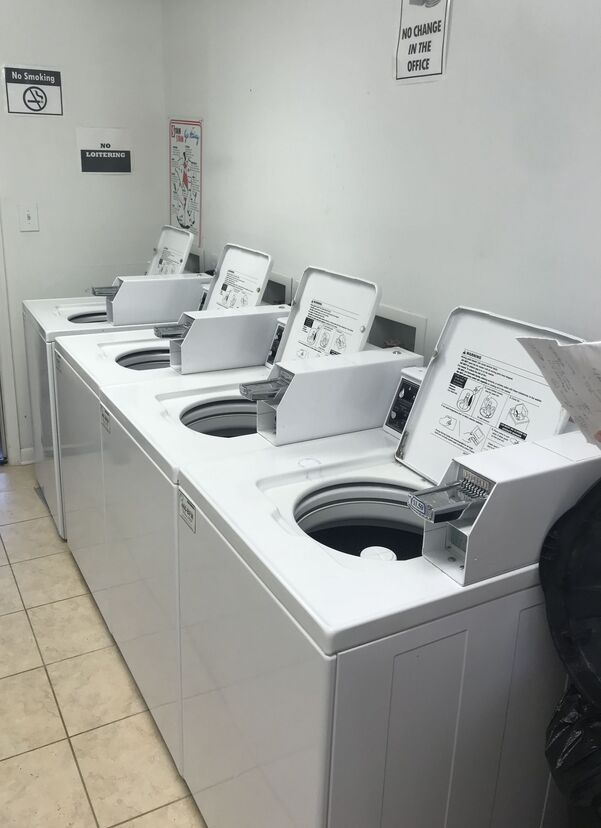 Row of white washing machines in a laundromat, lids open, instructions visible.