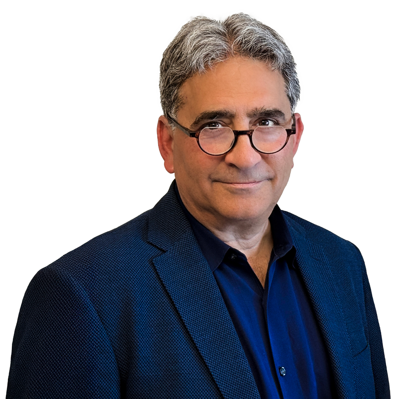 A man wearing glasses is smiling in front of a brick wall.