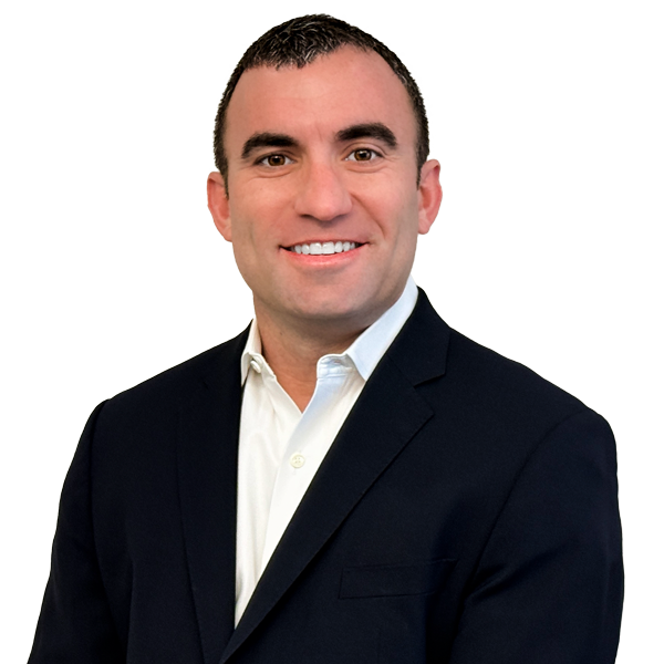 A man wearing glasses is smiling in front of a brick wall.