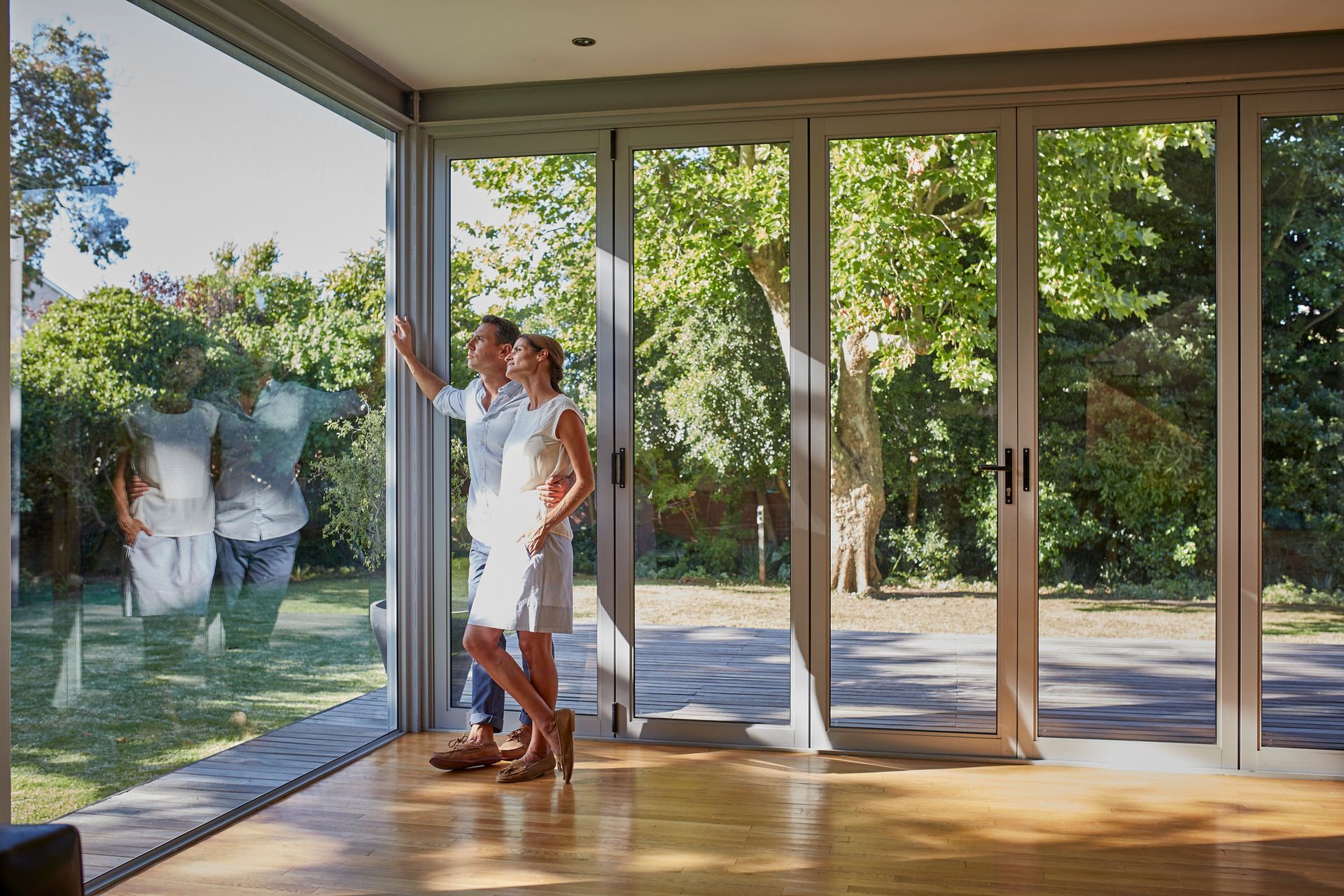 A man and a woman are standing in a living room looking out of a window.