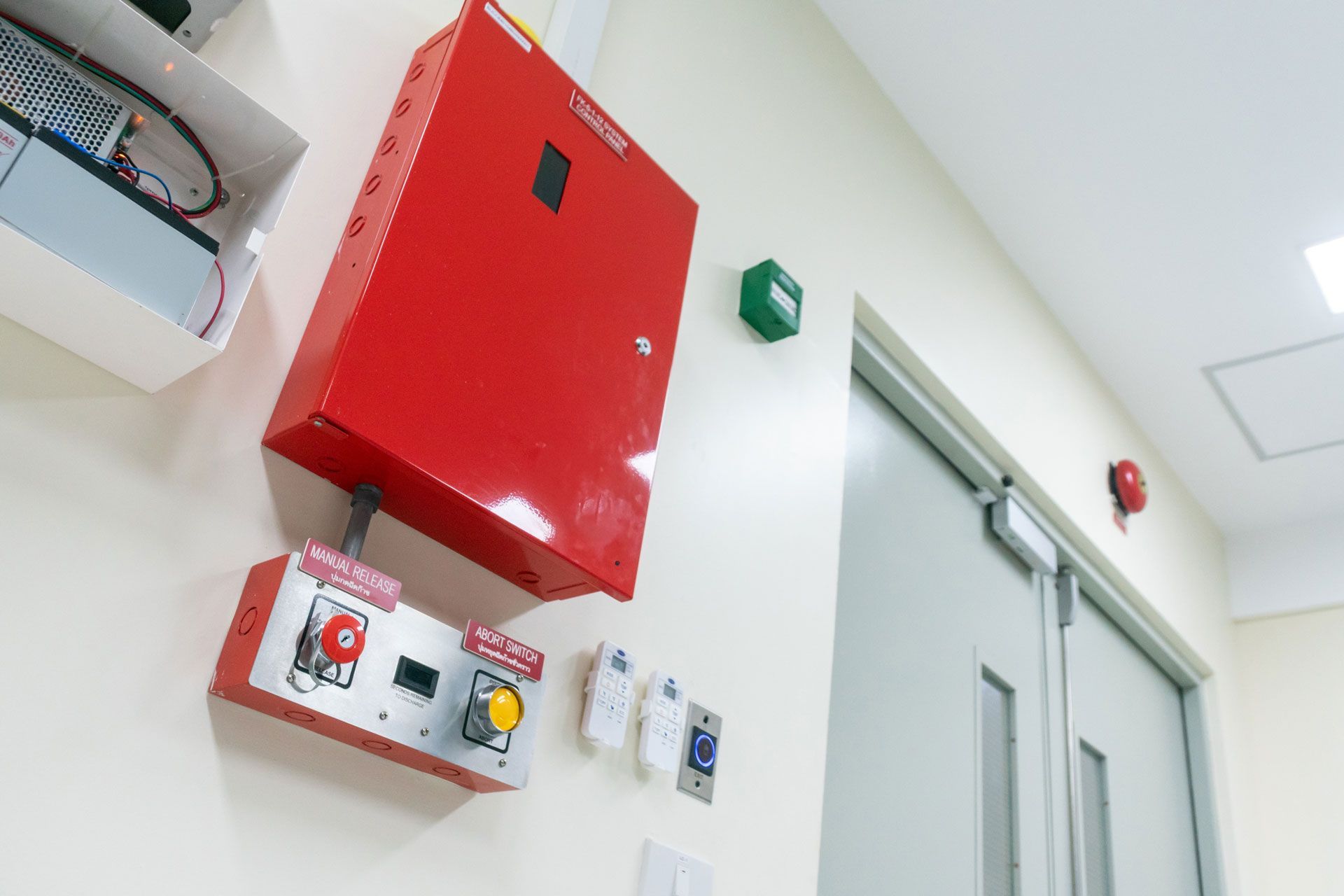 Red fire alarm panel and control box on wall next to a door.
