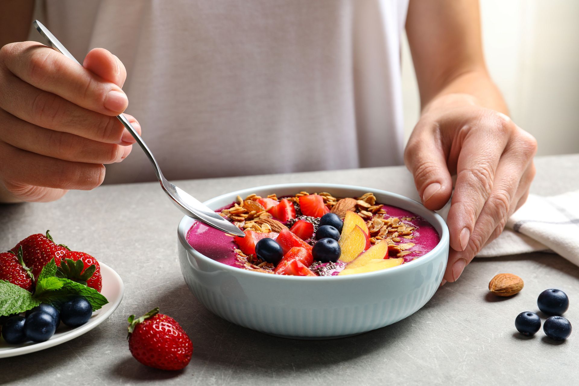 A person is eating a bowl of cereal with berries and granola