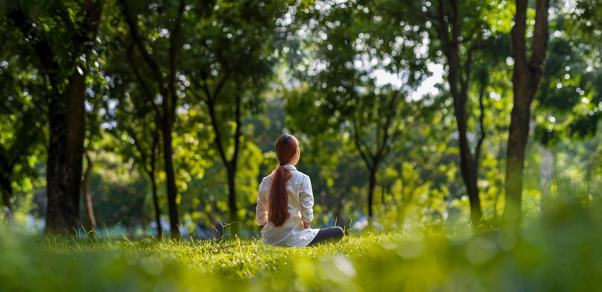 A woman is sitting in a lotus position in the middle of a forest