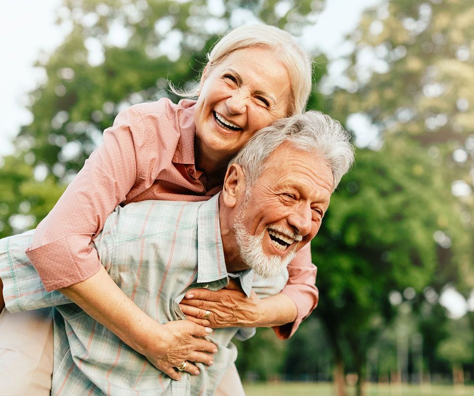 Elderly couple in a park, woman playfully riding on man's back.