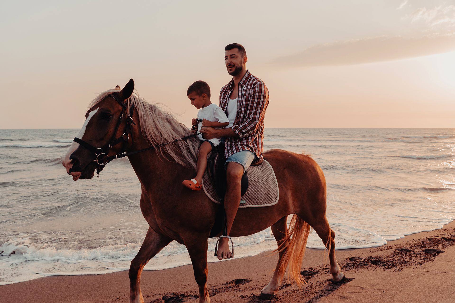 A man and a child are riding a horse on the beach