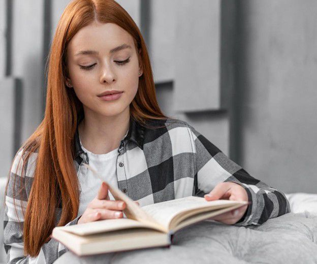 A young woman is sitting on a couch reading a book.